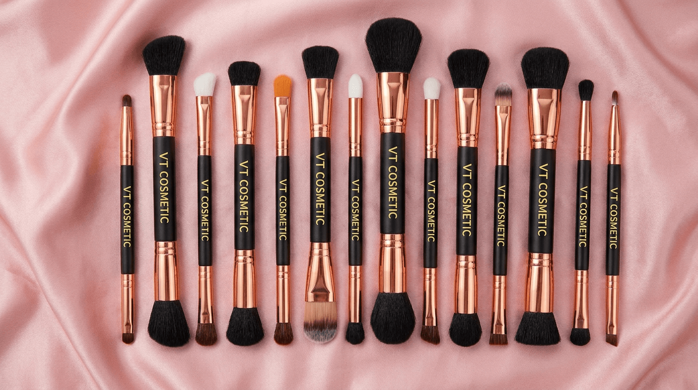 A collection of dual-ended makeup brushes with rose gold ferrules and black handles displayed on pink silk fabric